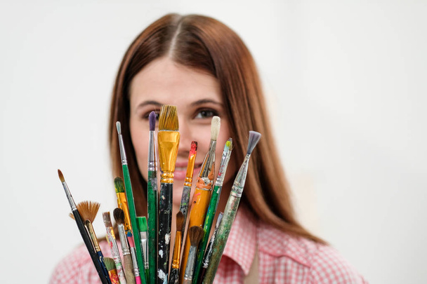 Young woman artist with brushes and paints in a white studio. - Photo, Image