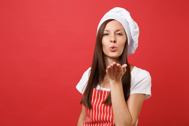 Housewife female chef cook or baker in red striped apron, white t-shirt, toque chefs hat isolated on red wall background. Close up portrait of housekeeper brunette woman. Mock up copy space concept - Photo, image
