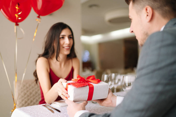 バレンタインデーのコンセプトです。恋に幸せなカップル。レストランでバレンタインデーを祝う、若い夫婦。恋人は互いに贈り物を与えます。バレンタインデーの概念のためのロマンスのレストラン. - 写真・画像