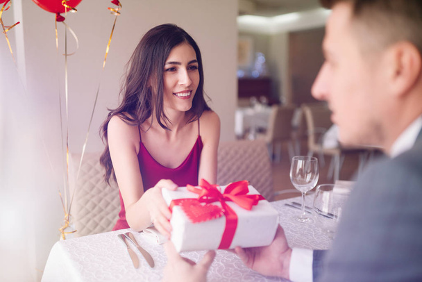 Valentine's Day concept. Happy couple in love with. A young loving couple celebrating Valentine's Day in the restaurant. Lovers give each other gifts. Romance restaurant for Valentine's Day- concept. - Фото, изображение