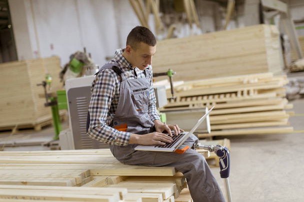 Behinderter junger Mann mit künstlichem Bein arbeitet in der Möbelfabrik - Foto, Bild