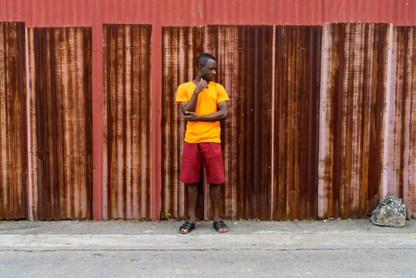 Young black African man thinking and looking down while standing - 写真・画像