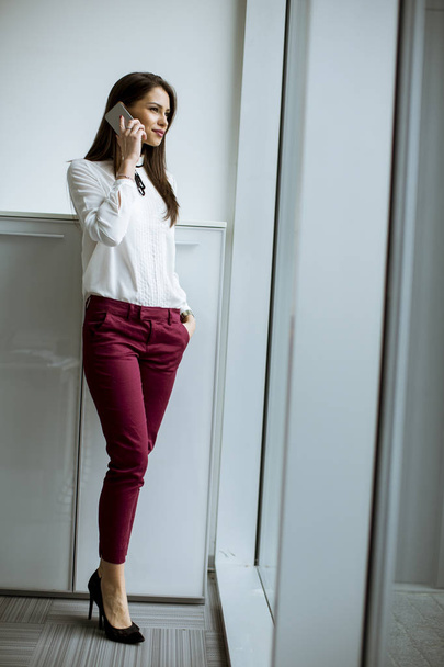 Young businesswoman standing in the office and  using mobile phone - Foto, Imagem