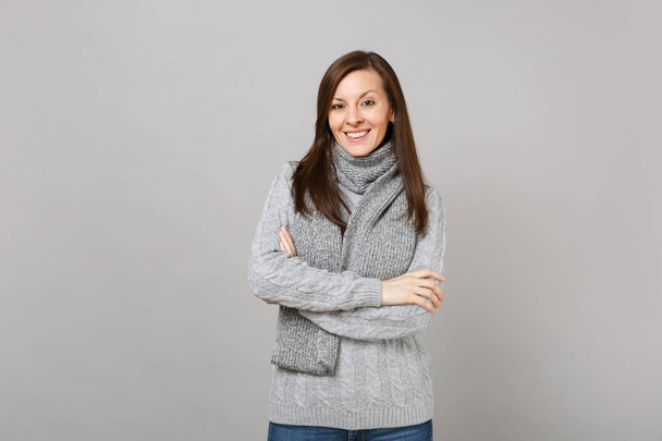 Giovane donna in maglione grigio, sciarpa che tiene le mani piegate isolata su sfondo grigio parete, ritratto in studio. Stile di vita sano, persone emozioni sincere, concetto di stagione fredda. Falsificare spazio di copia
 - Foto, immagini