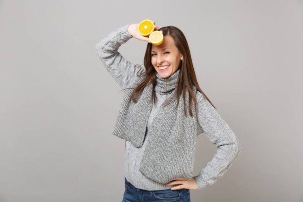 Smiling young woman in gray sweater, scarf holding lemon, orange isolated on grey wall background in studio. Healthy fashion lifestyle, people sincere emotions cold season concept. Mock up copy space - Foto, Bild