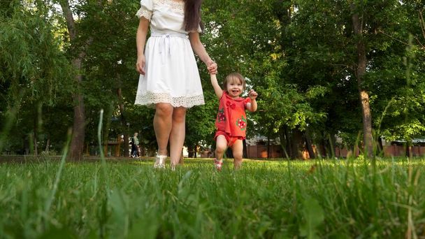 ребенок и мать ходить по зеленой траве газона в летнем городском парке и улыбаясь
. - Фото, изображение