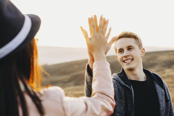 Handsome young guy smiling and giving high five to anonymous girlfriend while standing on background of field together.Cheerful man high fiving with girlfriend in meadow - Foto, Imagem