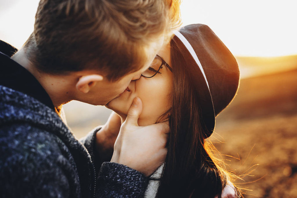 A fiatalember megcsókolta szenvedélyesen állva szép barátnője elmosódott háttér a természet naplemente alatt. Fiatal pár csókolózás vidéken - Fotó, kép
