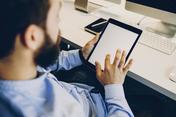 Növény bearded srác megható üres képernyő modern tabletta pultnál modern irodában ülve. Névtelen irodai dolgozó segítségével tabletta - Fotó, kép