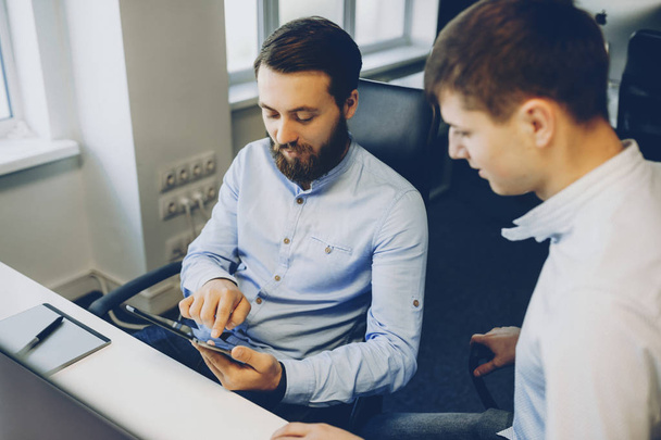Deux hommes en chemises élégantes assis au bureau et naviguant ensemble tablette moderne.Collèges masculins utilisant la tablette ensemble
 - Photo, image