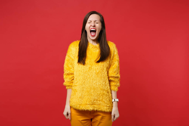 Portret dziwne szalone młode kobiety w futro żółty sweterek utrzymanie oczy zamknięte, krzyczy na białym tle na tle jasne czerwone ściany w studio. Koncepcja życia szczere emocje ludzi. Makieta do miejsca kopiowania - Zdjęcie, obraz