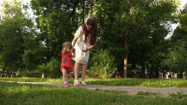Maminka a malá dcerka jdou podél cesty v letním parku. Babys první kroky s mámou - Fotografie, Obrázek
