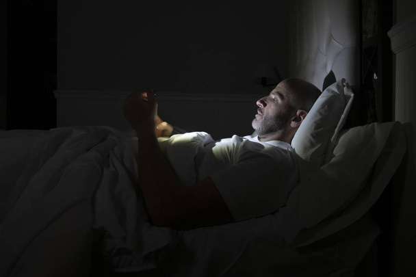 Man using his phone in his bed instead of sleeping, technology addiction concept - Fotó, kép