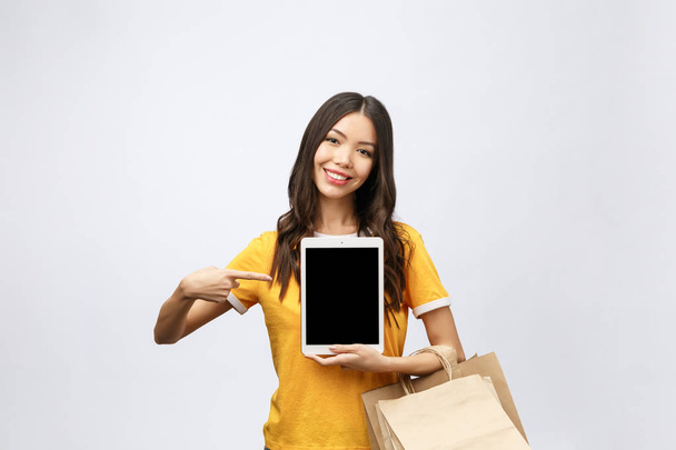 Portrait of woman in summer dress holding packages bags with purchases after online shopping, using tablet pc pad computer isolated on white background. Copy space for advertisement - Photo, Image