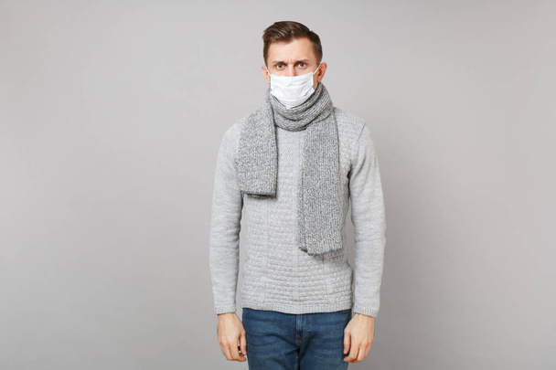 Young man in gray sweater, scarf with sterile face mask standing isolated on grey background, studio portrait. Healthy lifestyle, ill sick disease treatment, cold season concept. Mock up copy space. - Fotografie, Obrázek