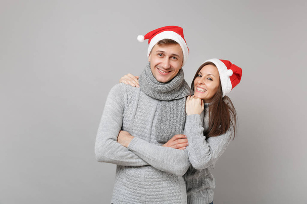 Feliz diversión pareja chica chico en rojo Santa Navidad sombrero suéteres grises bufandas aisladas en fondo de pared gris, retrato de estudio. Feliz Año Nuevo 2019 celebración fiesta concepto. Simular espacio de copia
 - Foto, Imagen