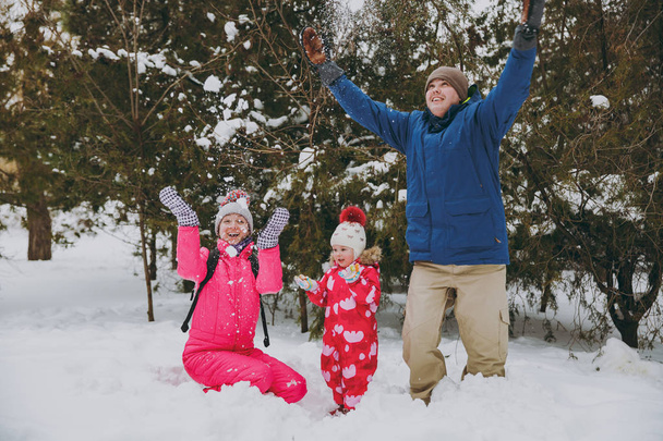 Счастливая семейная женщина, мужчина маленькая девочка в зимней теплой одежде играет, бросая снег в заснеженном парке или лесу на улице. Зимнее веселье, отдых в праздники. Концепция образа жизни семейных людей
 - Фото, изображение
