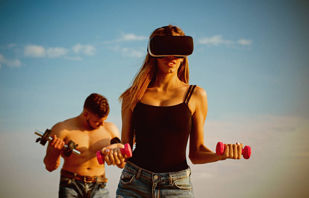 Virtual reality as training tool. Virtual reality simulator for fitness. Woman in virtual reality glasses build muscles with dumbbells. Virtual reality is here - 写真・画像