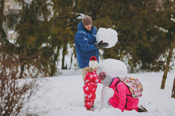 Mujer divertida de la familia, niña en ropa de abrigo jugando, haciendo muñeco de nieve, hombre sosteniendo bola de nieve en el parque o el bosque al aire libre. Diversión de invierno, ocio en vacaciones. Amor relación familia estilo de vida concepto
 - Foto, imagen