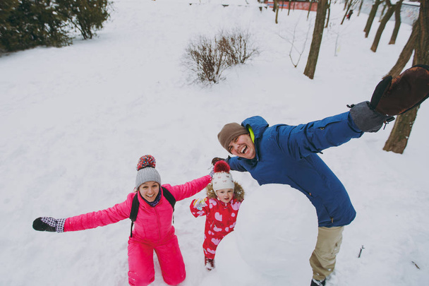 Веселий сімейний чоловік, жінка маленька дівчинка в теплому одязі грає, робить сніговика, розсовуючи руки в парку або лісі на відкритому повітрі. Зимові розваги, дозвілля у відпустці. Концепція сімейного способу життя любові
 - Фото, зображення
