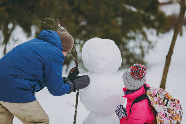 カップル女性、冬暖かい服プレイ、雪の公園または森林の外で雪だるまを作る男の背面をバックアップします。冬の楽しみ、休日レジャー。愛の関係家族の人々 のライフ スタイルのコンセプト - 写真・画像