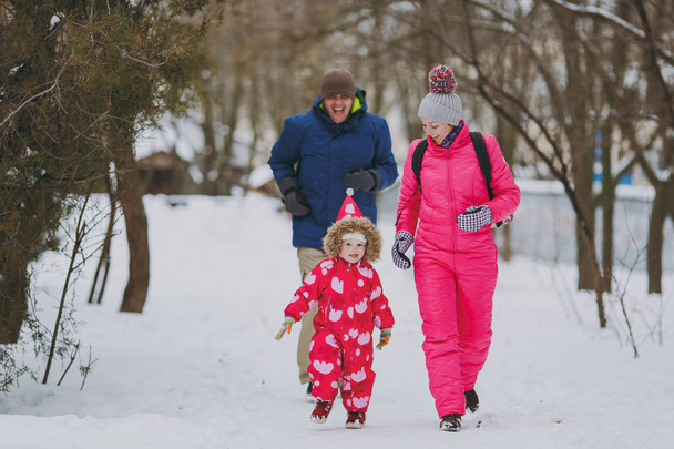 Radosny rodzina Kobieta, mężczyzna i dziewczynka w ciepłe ubrania uruchomiona spaceru w snowy park lub lasu na zewnątrz. Zimowe zabawy, wypoczynku na wakacjach. Miłość dzieciństwa relacji rodziny osób lifestyle concept - Zdjęcie, obraz