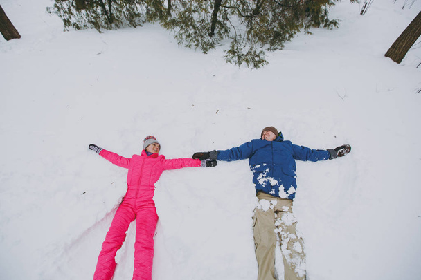 Mujer alegre pareja, hombre en ropa cálida de invierno colorido haciendo ángeles de nieve mientras está acostado en el parque o el bosque al aire libre. Ocio divertido de invierno en vacaciones. Amor relación familia gente estilo de vida concepto
 - Foto, imagen
