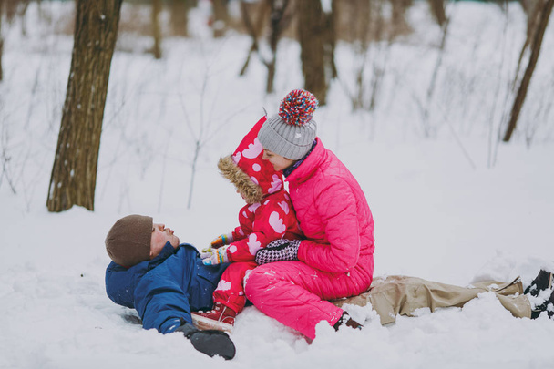 Happy family woman, man and little girl in warm clothes lying, sitting on snow in park or forest outdoors. Winter fun, leisure on holidays. Love childhood relationship family people lifestyle concept - Photo, Image