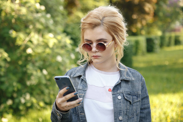 girl with round glasses. Hair in a bun. The girl with the phone. Girl looking - Фото, изображение