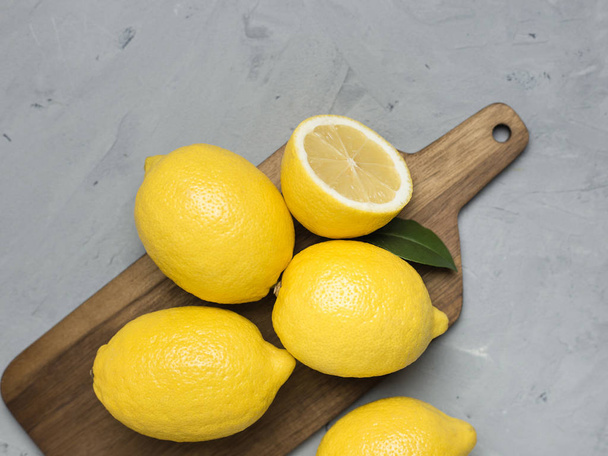Whole and sliced lemons on wooden cutting board. Organic fresh citrus fruits, top view, copy space. - Foto, afbeelding