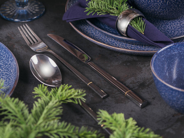 Christmas table setting. Dark blue decoration with fir-tree branch. Plates, wine glasses and cutlery with decorative textile on dark background. - Φωτογραφία, εικόνα
