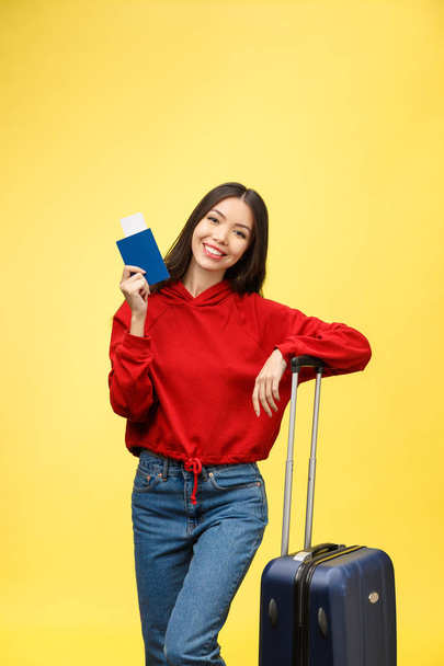 Woman travel. Young beautiful asian woman traveler with suitcase and passport on yellow background - Fotoğraf, Görsel