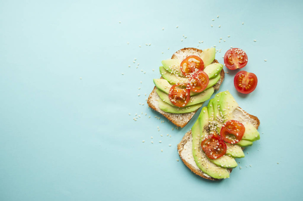 Poser à plat de délicieux toasts à l'avocat tranché, tomates et graines de sésame sur fond bleu avec copyspace
. - Photo, image