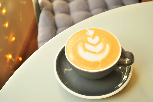 Una taza de café con hermoso arte latte en una mesa de madera gris en un café
. - Foto, Imagen