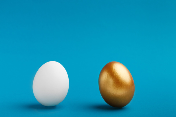 Ovos brancos e dourados sobre fundo azul, espaço de cópia
 - Foto, Imagem