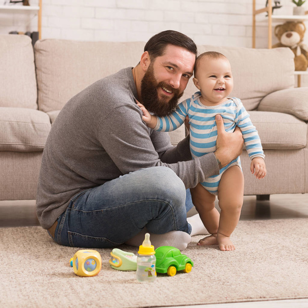Счастливый отец играет со своим маленьким сыном с яркой погремушкой
 - Фото, изображение