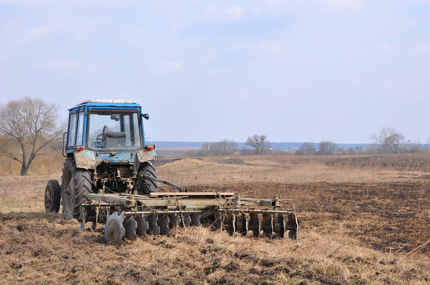 Пустой голубой трактор с ржавой бороной на поле ранней весной
 - Фото, изображение