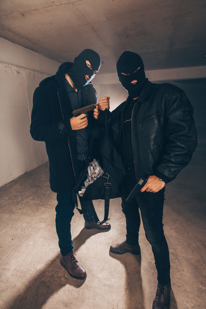 Assaulters stojící v temné místnosti se zbraněmi a ukradené peníze - Fotografie, Obrázek