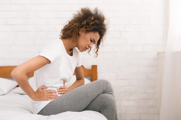 Ongelukkige vrouw last van buikpijn, zittend op bed - Foto, afbeelding