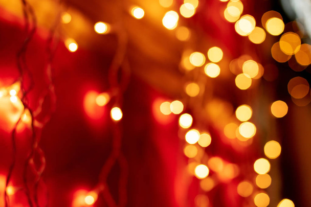 Rode bokeh wazig lights achtergrond. Gouden slingers versiering voor de nieuwe jaarviering. - Foto, afbeelding