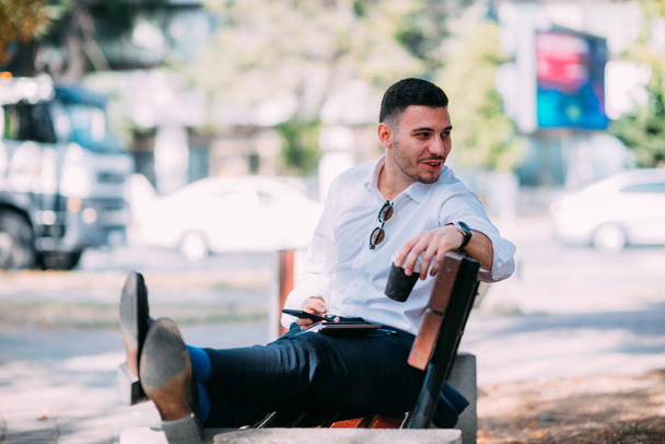 Empresário urbano está sentado no banco no centro da cidade, sorrindo e relaxando após o longo dia difícil
. - Foto, Imagem