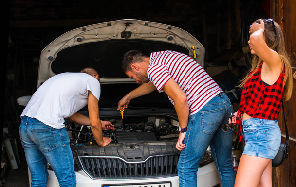 Two guys trying to fix some car troble while a girl is standing next to them - Photo, image