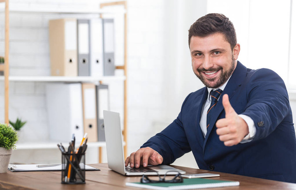 Бизнесмен показывает большой палец вверх, используя ноутбук в офисе
 - Фото, изображение