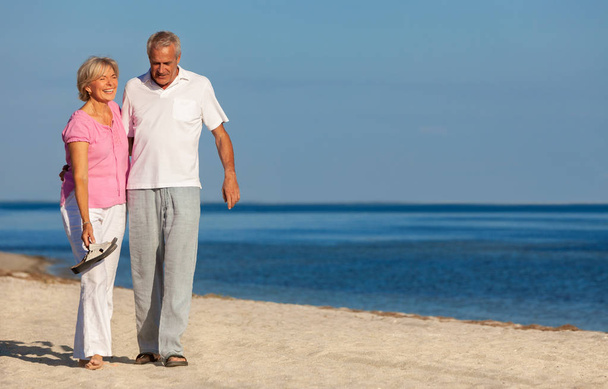 Feliz pareja de hombres y mujeres mayores caminando riendo de vacaciones en una playa tropical desierta con cielo azul claro brillante y mar tranquilo
 - Foto, Imagen