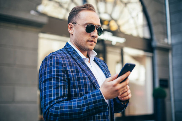 Κοντινό πορτραίτο ενός άντρα. επιχειρηματίας που κρατάει τηλέφωνο. φορώντας ένα μπλε σακάκι και ένα λευκό πουκάμισο. απασχολημένος. - Φωτογραφία, εικόνα