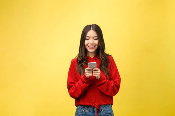 Young beautiful happy woman using smart phone. Isolated on yellow background - Foto, afbeelding