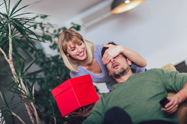 Happy man receiving a present from his girlfriend while sitting on the sofa - Φωτογραφία, εικόνα