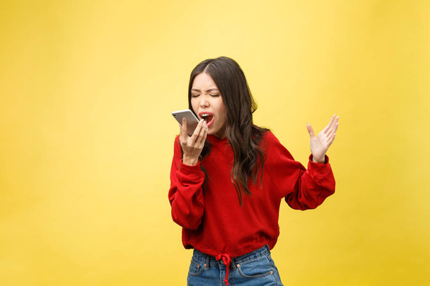 Portret wściekły młoda azjatycka kobieta rozczarować na telefon komórkowy podczas stania na żółtym tle - Zdjęcie, obraz