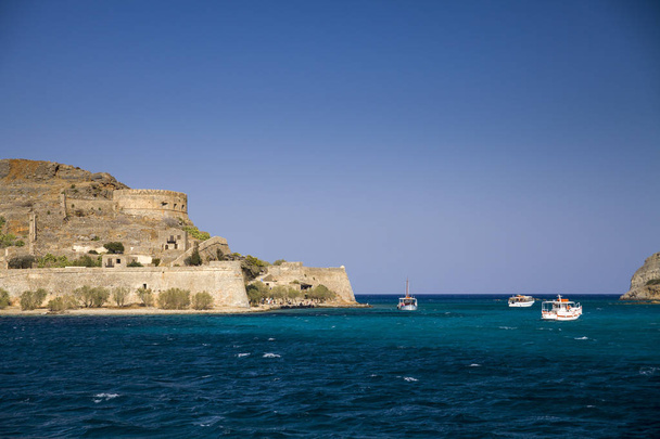 スピナロンガ島へのクルーズします。青いラグーンに小型ボート。スピナロンガ クレタ島、ギリシャの島の要塞。島のアーキテクチャ. - 写真・画像