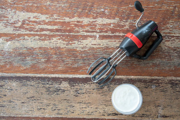 schwarz-roter Handrührbesen mit Schlagsahne für hausgemachte Butter auf Holzgrund. - Foto, Bild